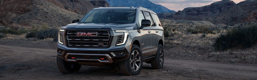Gray GMC SUV parked on a rugged desert trail with rocky canyon cliffs in the background at dusk.